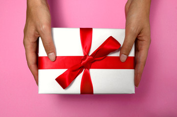 Gift in female hands on a colored background top view. gift box in women's hands flat lay. Female hands holding present with red bow. Festive backdrop for holidays: Birthday, Valentines day, Christmas