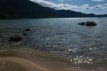 Late afternoon sunlight stricks the boulders and sandy beach in Lake Tahoe