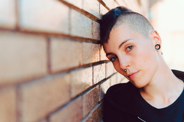 Young and attractive girl with shaved head and piercings. He has his head resting on a brown brick...
