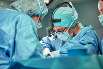 Group of surgeons looking at patient on operation table during their work - obrazy, fototapety, plakaty