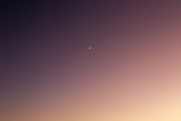 Evening sky going from purple to light orange with waxing crescent moon