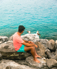 Woman sitting and watching two beautiful blue footed boobie birds. Natural wildlife shot in San Cristobal, Galapagos. Boobies bird on rocks with ocean sea background. Wild animal in nature. Holiday