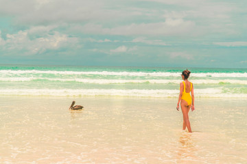 Yellow bikini Woman on beach. Tourist walking along Tropical Galapagos beach with turquoise ocean waves and white sand. Holiday, vacation, paradise, summer vibes. Isabela, San Cristobal