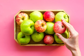 Healthy diet concept. Fresh apples in tray, hand hold apple, pink background top view