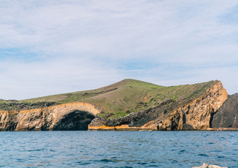 Beautiful landscape natural rock arch, on cliff edge shoreline. Caves. Orange rock with green and blue ocean background. Shot on expedition off Isabela island, Galapagos, Ecuador.