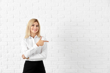 Beautiful stylish businesswoman pointing at something against white brick wall