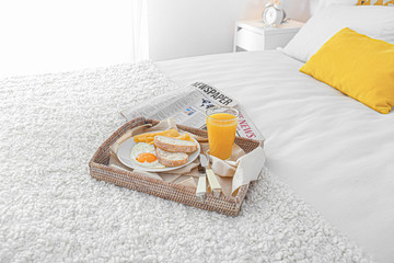 Tray with tasty breakfast and newspapers on bed