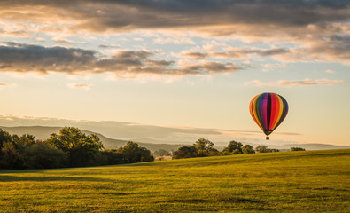 Rainbow hot-air balloon floats over valley at sunrise