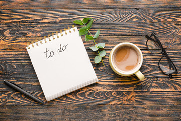 Notebook with text TO DO, cup of coffee, pen and glasses on wooden background