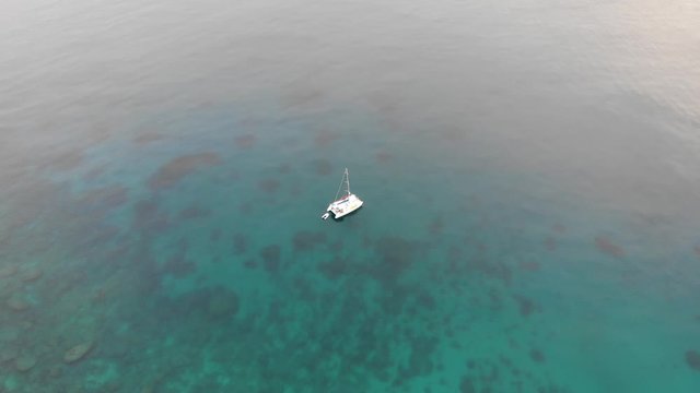 Aerial view of a catamaran yacht anchored in clear blue water and coral reef off a tropical island in the south pacific