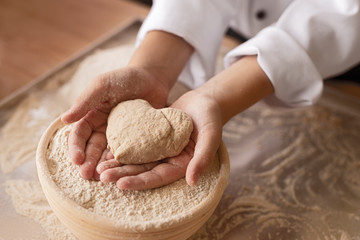 Crop kid showing dough heart in bakery