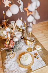 New Year mood, Christmas tree. Rectangular table covered with a gold tablecloth, decorated with candles with flowers for celebration. Festive still life by candlelight.