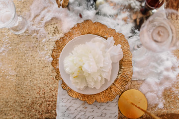 New Year mood. Table with a gold tablecloth, decorated with candles for celebration. Festive still life by candlelight. Beautiful calligraphy with a flower on a plate. Top view.