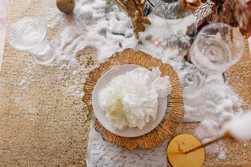 New Year mood. Table with a gold tablecloth, decorated with candles for celebration. Festive still life by candlelight. Beautiful calligraphy with a flower on a plate. Top view.