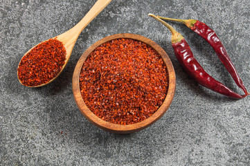 Top view red dried crushed hot chili peppers and chili flakes or powder in wooden spoon and bowl on grey rustic background, healthy turkish spice