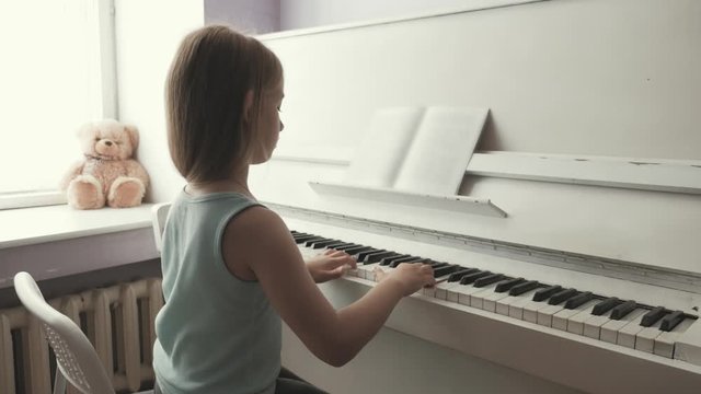 Little girl studying to play the piano at home. Preschool child having fun with learning to play music instrument. Education, skills concept.