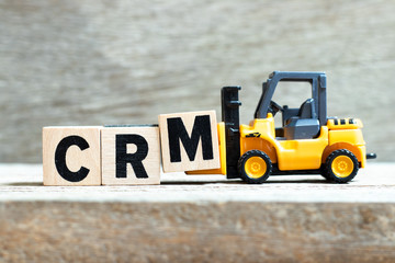 Toy forklift hold letter block M to complete word CRM (Abbreviation of Customer Relationship Management) on wood background