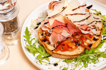 Italian Cuisine. Bruschetta with prosciutto tomatoes, ham, arugula and parmesan