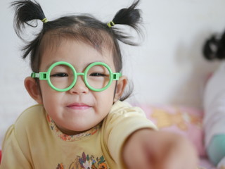 Little baby girl, 30 months old, with a plastic glasses on playing with / trying to touch a camera, while taken a photo