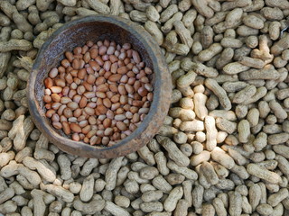 Peeled peanuts in a coconut shell on top of many harvested raw peanuts, being placed outdoor to dry them off