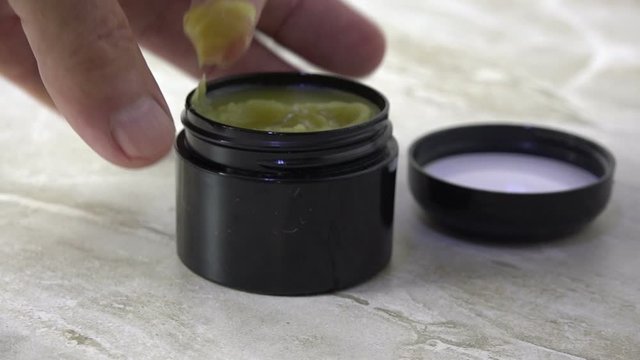 A finger dipping into a jar of CBD salve slow motion