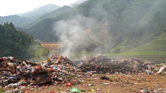 Stack of different types of large garbage dump, plastic bags, and trash burning near paddy rice terraces, agricultural fields of Mu Cang Chai, mountain in Vietnam in environmental pollution concept.