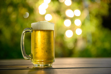 A glass of cold beer with a foam on top Placed on a table in the garden, the background is a green...