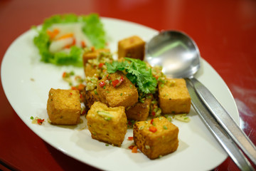 Stir-fried tofu, chili, salt, topped with coriander on a white plate on a red table in a Chinese restaurant in Thailand.