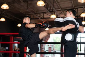 Young Asian Kick boxer kicking professional trainer in boxing studuim in the background at fitness...