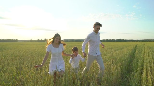 happy family outdoors running on wheat field with little boy. Mother, father, son child having fun on summer day enjoying nature together, health love travel summertime happy holiday happiness sunset