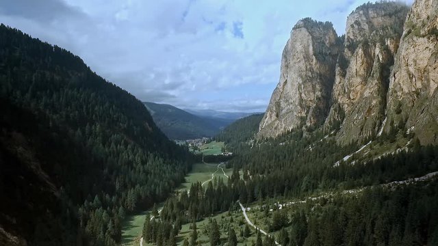 Grand vista of beautiful valley in the Alps. Rock towers, green meadows, dark forest and dramatic clouds in the sky.