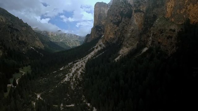 Dark and imposing view of a wild and rugged valley with high cliffs, dark forests and dramatic clouds in the sky.