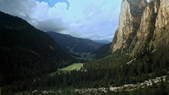 Sideways flight right to left across a beautiful alpine mountain valley with sheer rock on the right and wooded hills on the left.