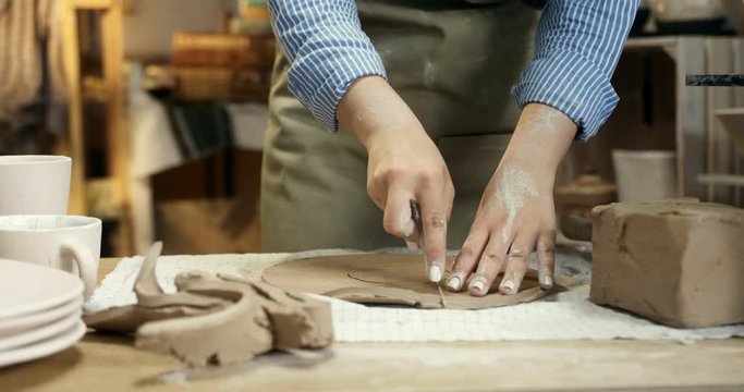 Close up of the hands of the female Caucasian potter dividing a clay in two parts for molding a ceramic item from it.