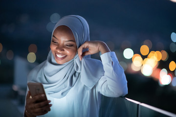 Young Muslim woman on  street at night using phone - Powered by Adobe