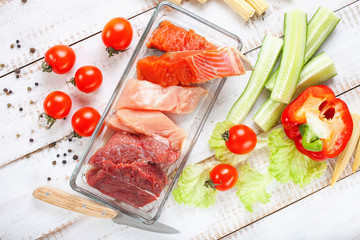 Products for a diet - raw meat of beef and chicken, a salmon and vegetables on a light wooden background. Selective focus.
