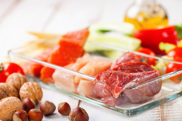 Products for a diet - raw meat of beef and chicken, a salmon and vegetables on a light wooden background. Selective focus.