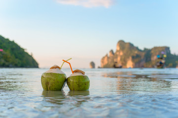 Two drinking coconut with straws on a tropical beach. - obrazy, fototapety, plakaty
