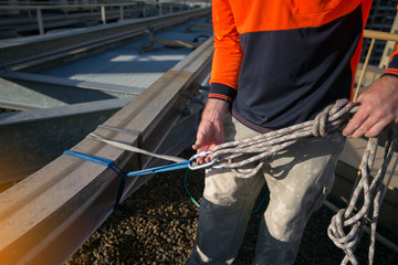 Rope access worker inspecting rope rigging on locking Karabiner its attached into safety 25 tone sling and bunny ears knot prior to used on structure beam roof top high rise building site, Sydney   