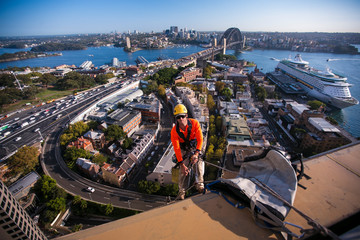 Industry rope access building repairer inspector wearing a safety helmet, working at height fall arrest position descending construction building site harbour bridge background, Australia    - Powered by Adobe
