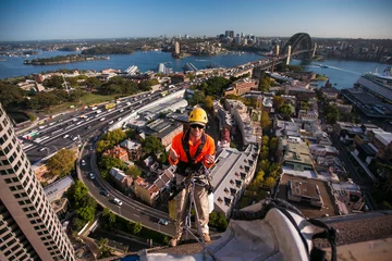 Poster Male rope access windows cleaner wearing safety hard hat, long sleeve shirt safety harness, carrying white bucket, working at height,  descending from high rise building Sydney city, Australia © Kings Access