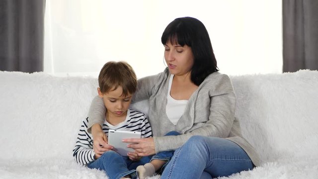 Happy family: mother and son spend time together playing or watching a movie on a tablet. The concept of the modern family and the relationship between millennial and Z.