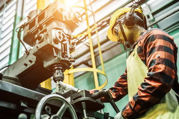 Asian worker wering the goggle, helmet, ear muff equipment in production plant using machine on the factory shop floor