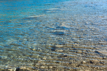 crystal clear blue cool water at the shore of a wild lake in a quarry without people with steep rocky beaches and large boulders on a summer warm day