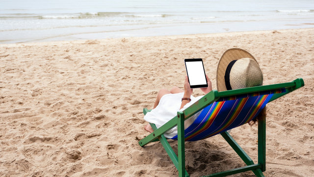 Mockup image of a woman holding a black tablet pc with blank desktop screen while lying down on a beach chair