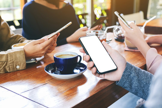 Mockup image of a hand holding and using black mobile phone with blank desktop screen with friends in cafe