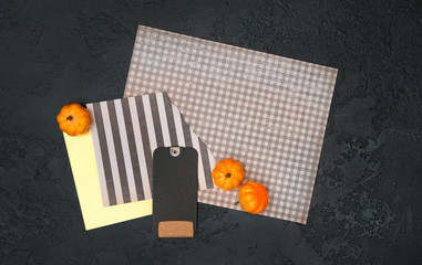 creative backround with paper blank and pumpkin. paper, black tag and pumpkins on abstract black background. fall time concept. flat lay. mock up