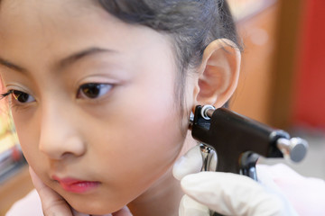 Adorable little Asian girl having ear piercing process. - 295228217