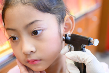 Adorable little Asian girl having ear piercing process. - 295228220