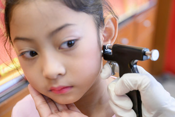 Adorable little Asian girl having ear piercing process. - 295228243